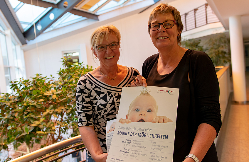 Angelika Uhlen und Kornelia Böert (von links) weisen auf den Markt der Möglichkeiten zum Thema „Frühe Hilfen“ in den Familienzentren hin.